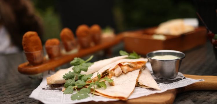 Close-up of savory quesadillas with coriander on a tray, served with dipping sauce.
