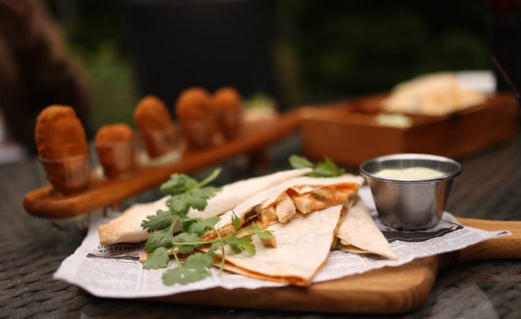 Close-up of savory quesadillas with coriander on a tray, served with dipping sauce.